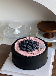 a black cake with pink frosting and blueberries on top sitting on a table