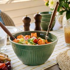 a green bowl filled with salad on top of a table next to plates and utensils