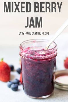 a mason jar filled with mixed berry jam next to strawberries and blueberries on the side