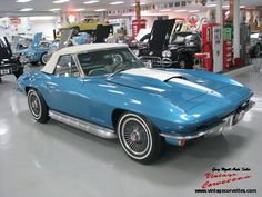 a blue and white car is parked in a showroom with other cars behind it