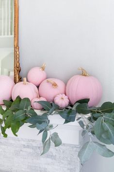 some pink pumpkins are sitting on top of a mantle with greenery and a mirror in the background