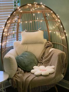 a wicker chair with pillows and blankets on it in front of a window covered by lights