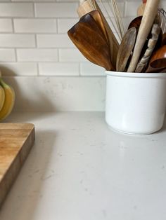 a white cup filled with wooden utensils on top of a counter next to bananas