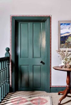 a green door in a white room next to a table with flowers and vases on it