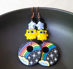 pair of earrings with cartoon characters hanging from hooks on black plate next to white background