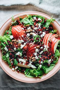 an apple and pomegranate salad in a pink bowl on top of a table