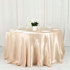 a round table with two vases and flowers on it in front of a white curtain