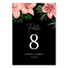 a table number card with pink flowers and leaves on black paper, in the shape of an eight