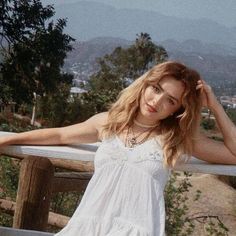 a beautiful young woman standing next to a wooden fence