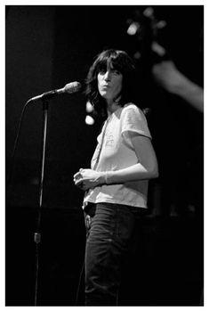 a black and white photo of a woman standing in front of a microphone on stage