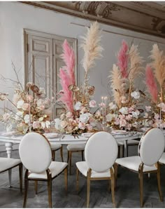 a dining room table set with white chairs and pink flowers