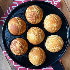 six pastries in a black pan on a red and white towel next to a wooden table