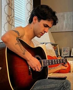 a man sitting on top of a bed holding a guitar in his right hand and looking down at the ground