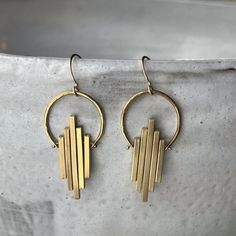 "These art deco dangles are clean and classy with a graceful swing to them, making them a perfect accessory for your dinner party or a dressy night out with the girls!  Using just a few spools of wire, some brass pieces, and a collection of specialized tools, we hammer, drill, melt, sand, and polish each individual piece until it becomes a wearable work of art. The 14k gold fill ear wires provide a luxurious touch and attach to a solid brass hand textured semi-circle. Below the circle, varying l Art Deco Round Pierced Earrings, Handmade Contemporary Drop Earrings, Handmade Contemporary Brass Jewelry, Contemporary Handmade Brass Jewelry, Art Deco Dangle Pierced Earrings, Contemporary Handmade Drop Earrings, Art Deco Sterling Silver Drop Earrings, Art Deco Sterling Silver Dangle Earrings, Contemporary Gold Long-drop Earrings