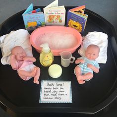 three baby dolls sitting in front of a bath tub with soap and books on the table