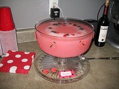 a pink drink in a bowl on a counter next to wine bottles and utensils