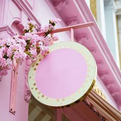 a pink and gold sign hanging from the side of a building with flowers on it