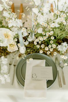 a place setting with white flowers and greenery