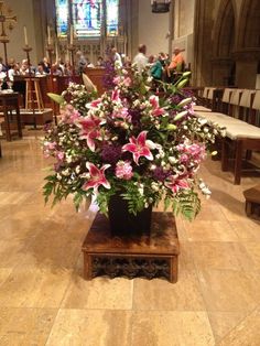 a vase filled with lots of flowers on top of a wooden table in a church