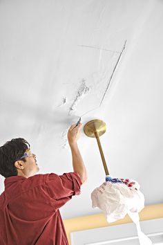 a man is painting the ceiling with white paint and a gold light fixture in his hand