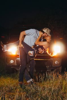 a man and woman kissing in front of a truck with the headlights on at night