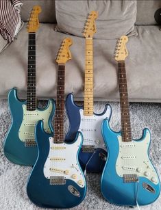 three electric guitars are lined up on the floor in front of a couch and pillows