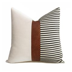 a white and brown pillow sitting on top of a wooden table next to a black and white striped pillow