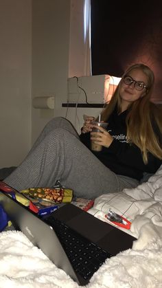 a woman sitting on a bed holding a drink in her hand and looking at the camera