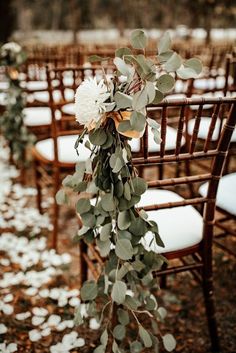 an outdoor ceremony with white flowers and greenery hanging from the back of wooden chairs