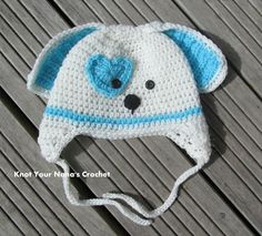 a crocheted white and blue hat with a bear on the front, sitting on a wooden surface