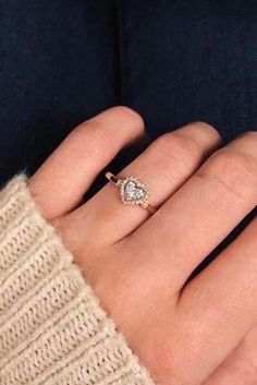 a woman's hand wearing a gold ring with a heart shaped diamond on it