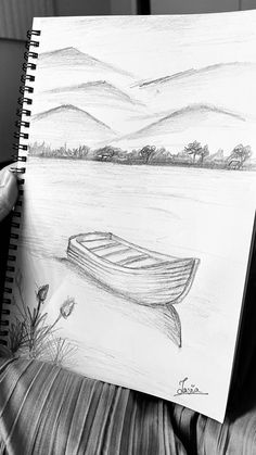 a person holding up a drawing of a boat on the water with mountains in the background