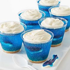 six blue dessert cups with white frosting and sprinkles on a tray