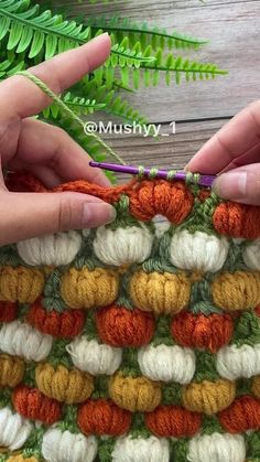 two hands are crocheting an orange and white granny's afghan with green leaves