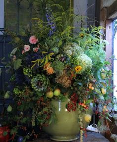 a large vase filled with lots of flowers and greenery on top of a table