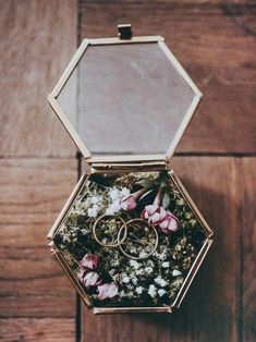 an open box with two wedding rings in it on a wooden floor next to flowers