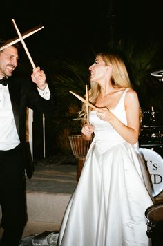 a man in a tuxedo and a woman in a white dress holding sticks