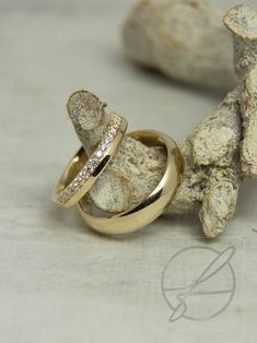 two gold wedding rings sitting on top of each other next to some rocks and driftwood