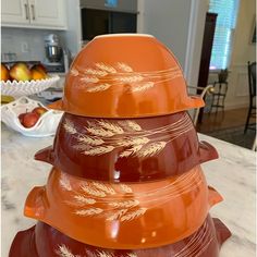 a stack of orange bowls sitting on top of a counter next to an apple bowl