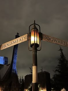 a lamp post with two street signs on it and a building in the background at night