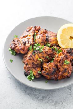 grilled chicken on a plate with lemon wedges and cilantro garnish