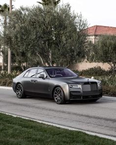 a silver rolls royce parked on the side of a road next to trees and bushes