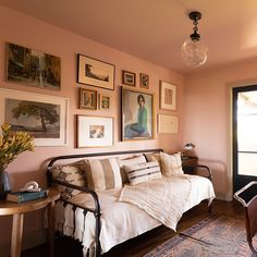 a living room with pink walls and pictures on the wall above the couch, along with a small table