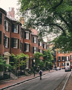 a man riding a bike down a street next to tall red brick buildings and trees