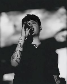 a man with tattoos on his arm holding a microphone to his ear and singing into a mic