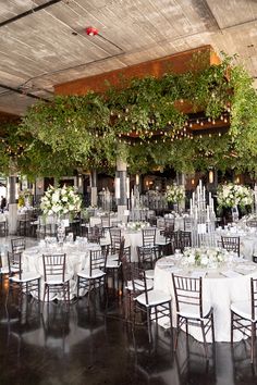 the tables are set with white linens and greenery hanging from the rafters