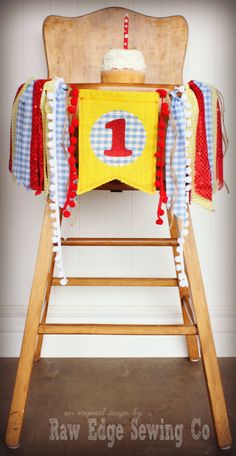 a wooden high chair with a birthday cake on it's top and red, white, and blue ruffles