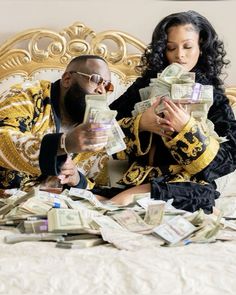 a man and woman sitting on a bed covered in money