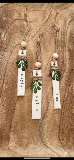 three white tags with green leaves are hanging on a wood surface, one has a name tag and the other has a wooden bead