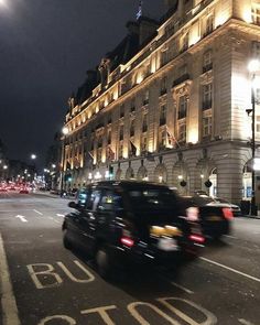 cars driving down the street at night in front of a large building with lights on